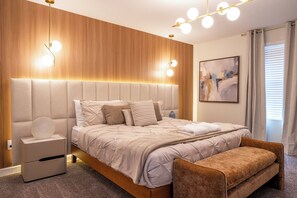 Une chambre à coucher moderne avec un grand lit, des tables de chevet, un banc et un tableau au mur.