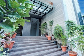 A hotel entrance with a staircase leading to the lobby, surrounded by potted plants.