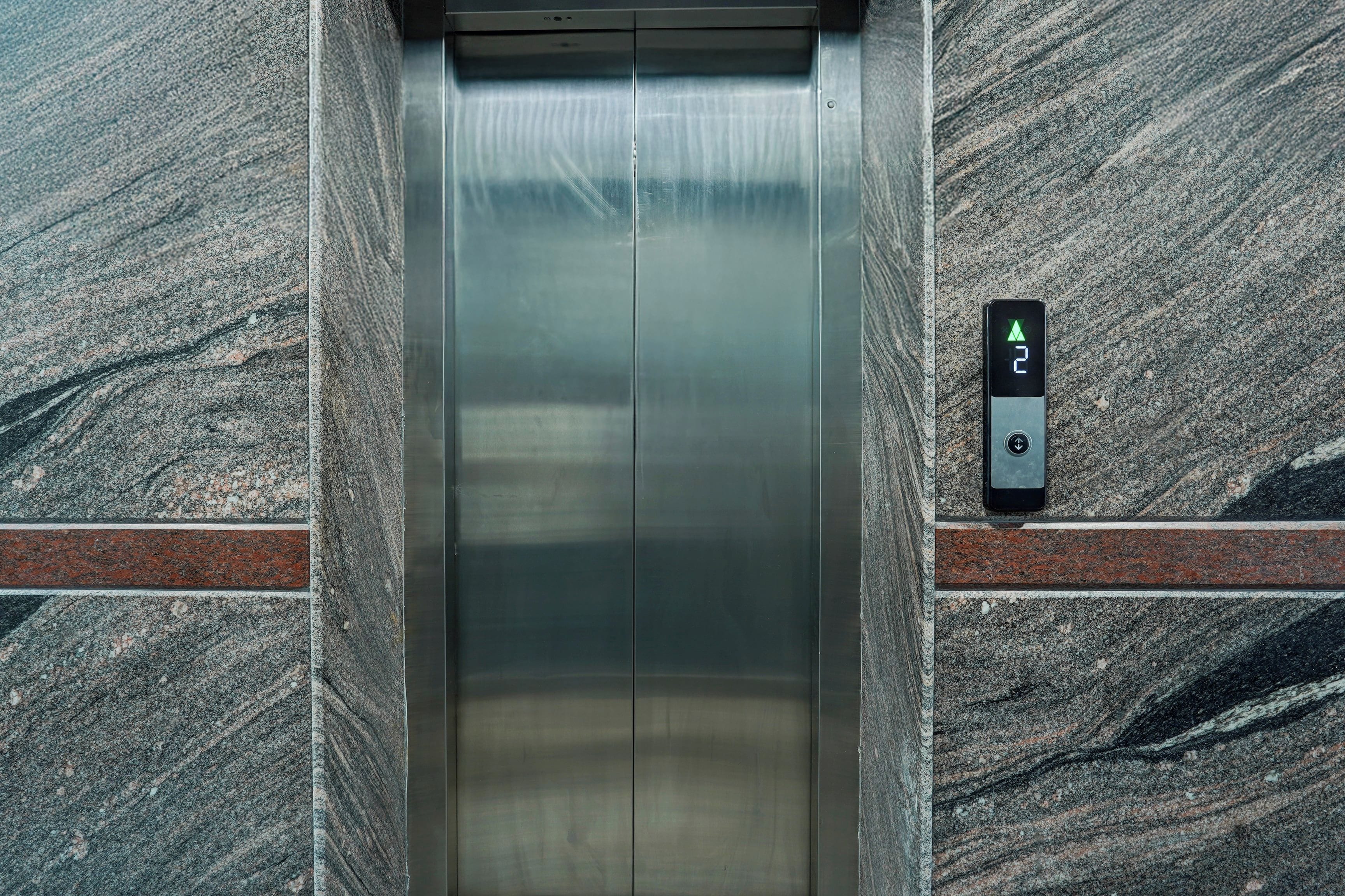 Un ascensor con pantalla digital y botones, rodeado de paredes de granito.