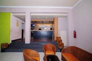 Zona de recepción de un hotel con mostrador, extintor y sillas de mimbre.