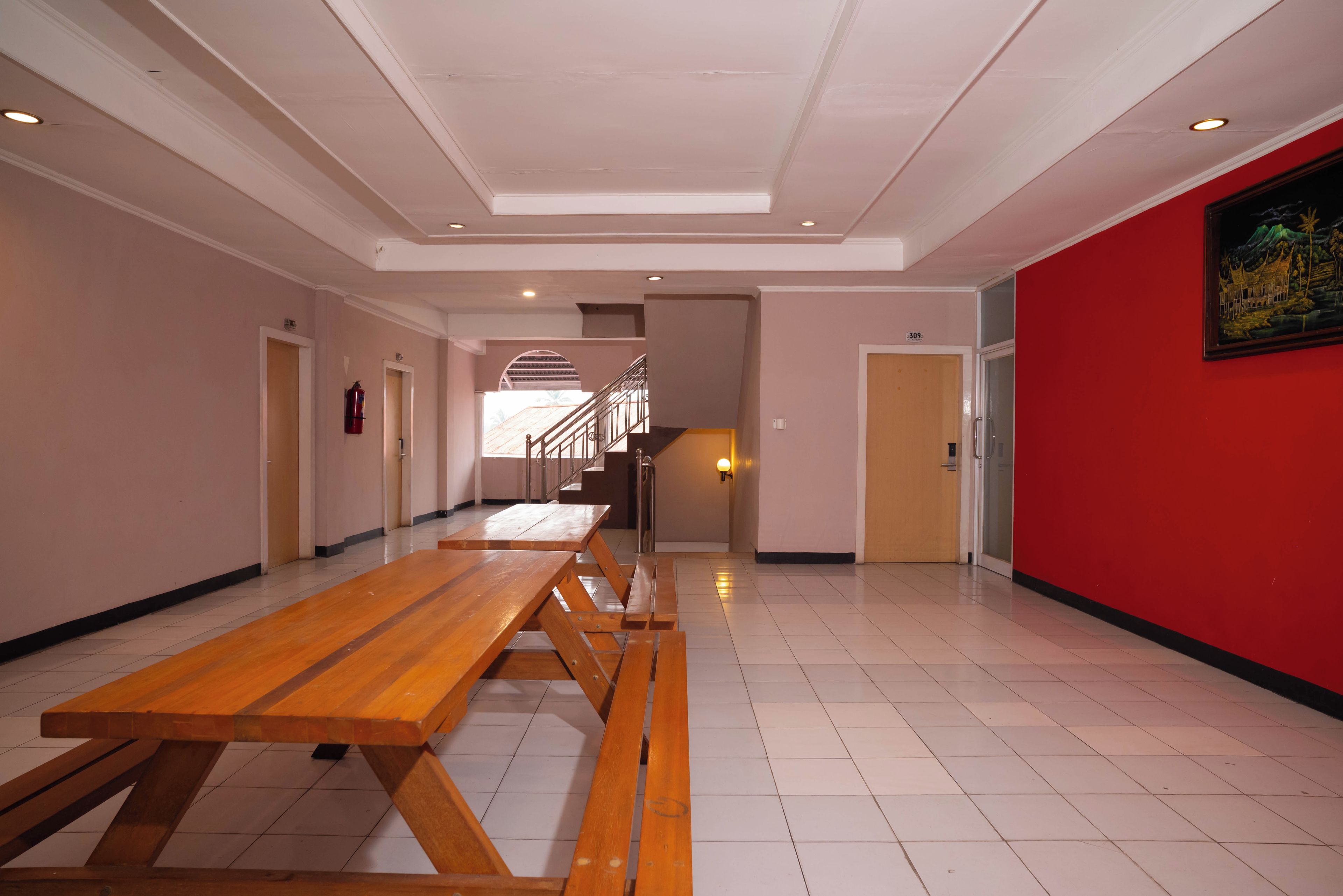 A spacious corridor with a wooden bench, a staircase, and a red wall with a framed picture.