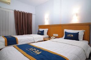 Habitación de hotel con dos camas, cada una con una colcha azul y amarilla que muestra el logotipo de AR3 Hospitality. Hay un teléfono en la mesita de noche entre las camas y la habitación tiene un cabecero de madera.