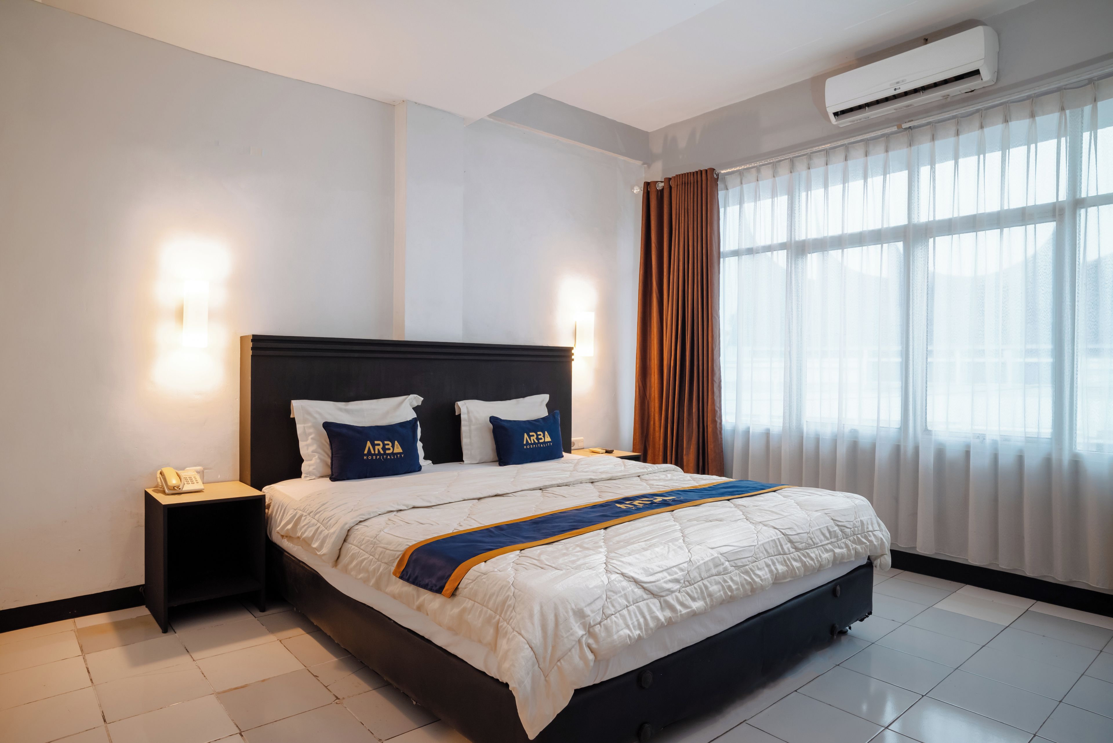 A hotel room with a large bed, a bedside telephone, and a window with curtains.