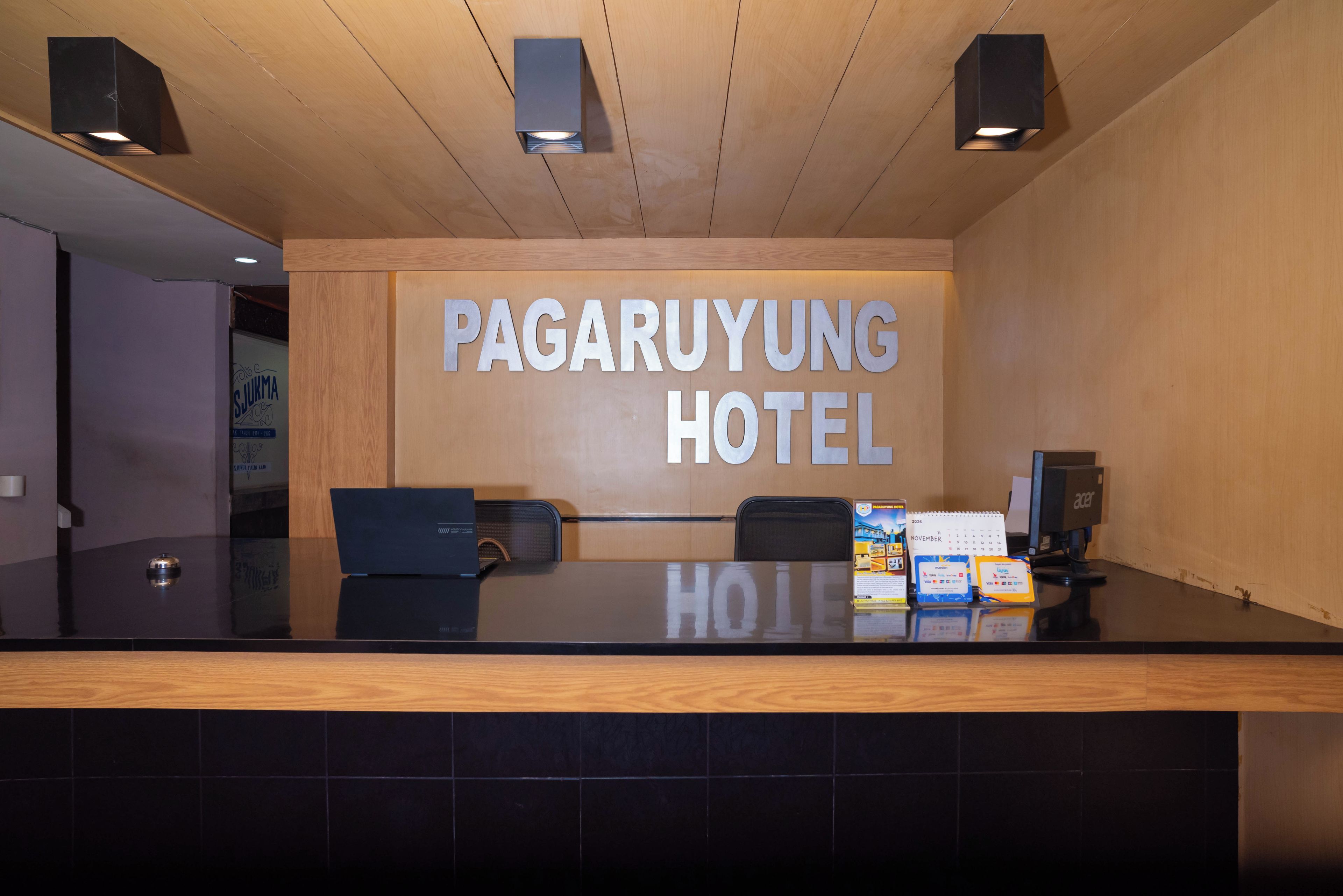 A reception desk with a wooden panel wall, a sign reading 'PAGARUYUNG HOTEL', and a calendar for November 2026.