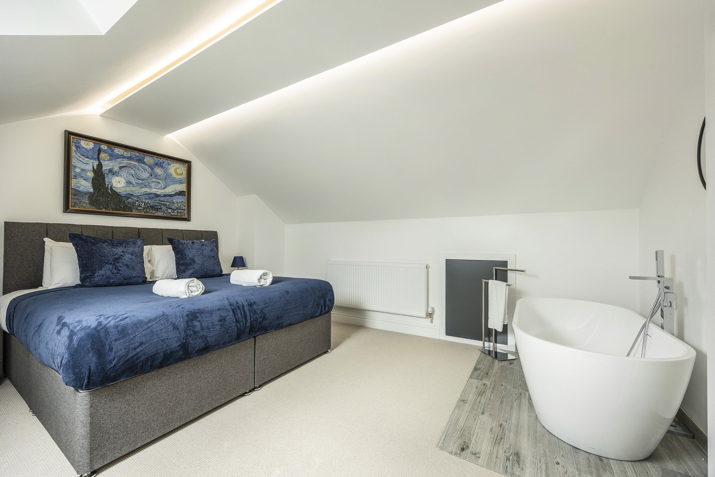 Een moderne slaapkamer met een groot bed, een schilderij, een witte badkuip en een radiator.