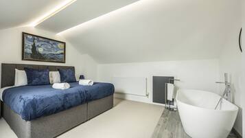 Een moderne slaapkamer met een groot bed, een schilderij, een witte badkuip en een radiator.