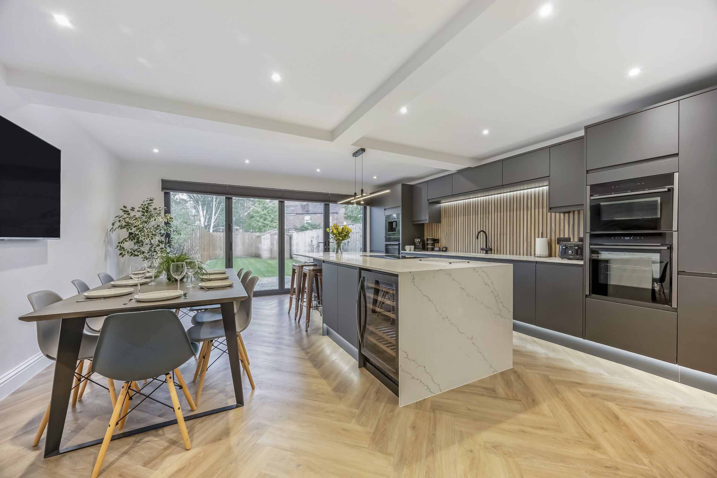 Une cuisine moderne dotée d’un îlot central, de meubles de couleur sombre et d’appareils électroménagers intégrés.