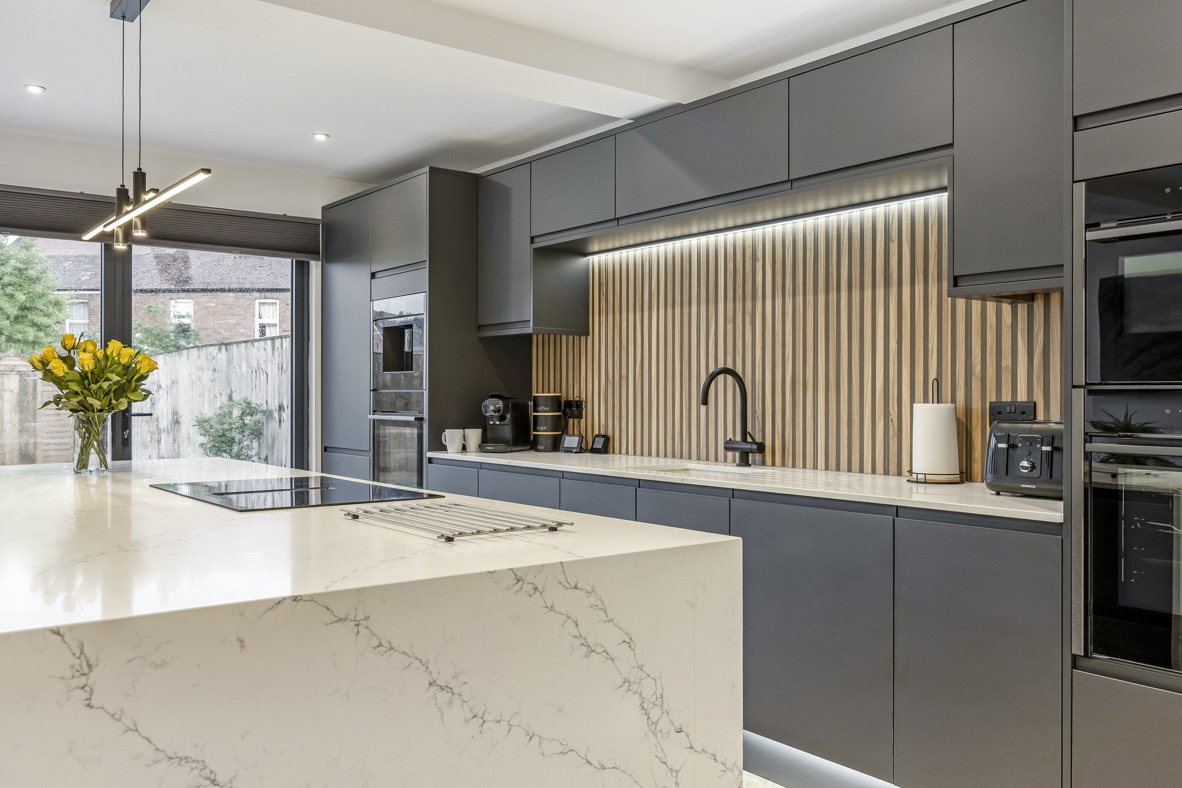A modern kitchen with a marble countertop, built-in appliances, and a vertical wood panel backsplash.