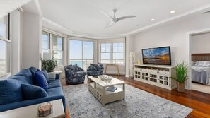 En moderne stue med sofa, lænestole, sofabord, fjernsyn og en balkon med udsigt.