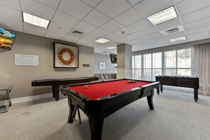 A pool table in a room with a large window, a fireplace, and a wall-mounted television. - Residence 709 at The Grand (Wildwood)