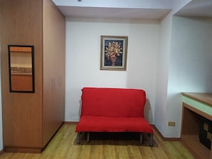 Een kamer met een houten garderobe, een rode bank en een ingelijst kunstwerk aan de muur.