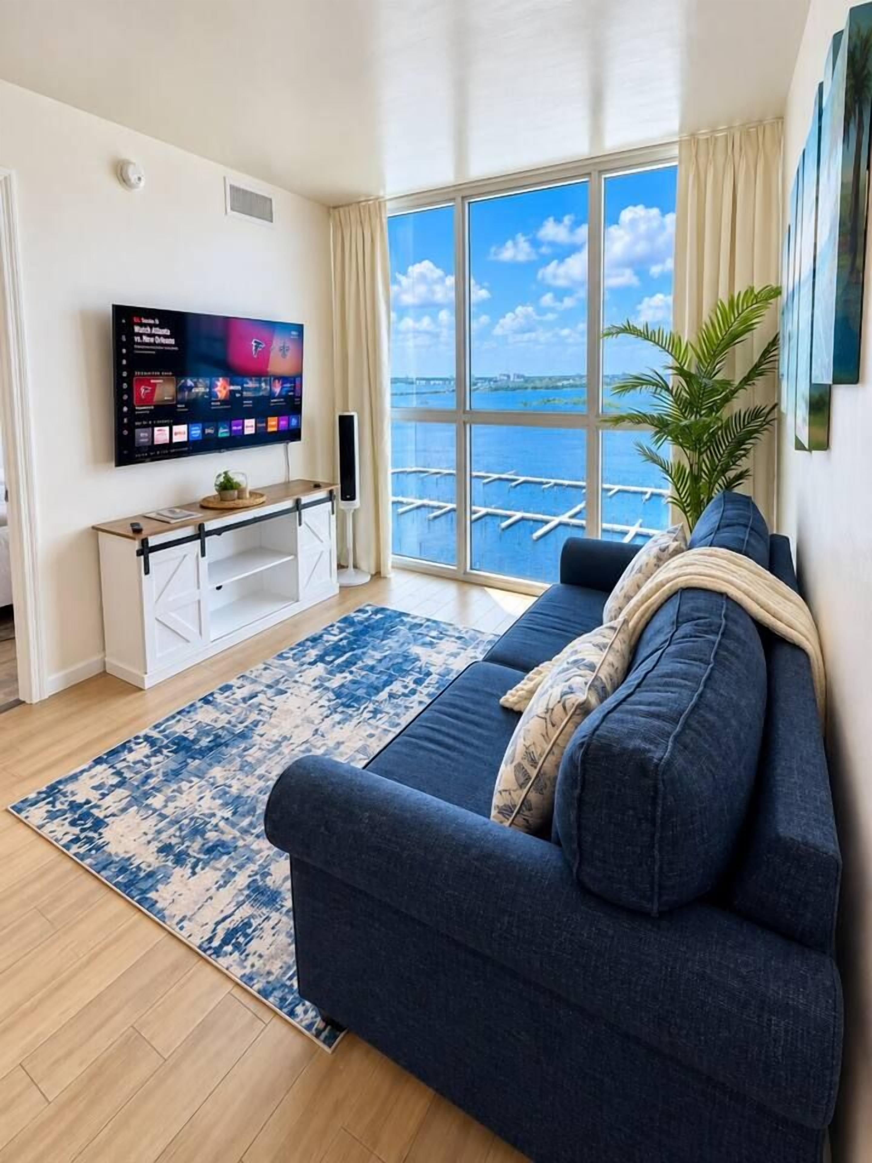A living room with a large window, a blue sofa, a flat-screen TV, and a wooden cabinet.