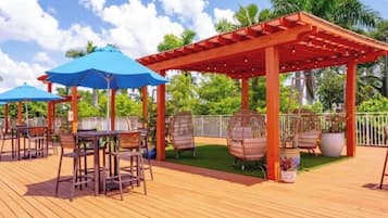 Eine Holzterrasse mit Außenmöbeln, darunter Tische und Stühle, sowie eine Pergola.