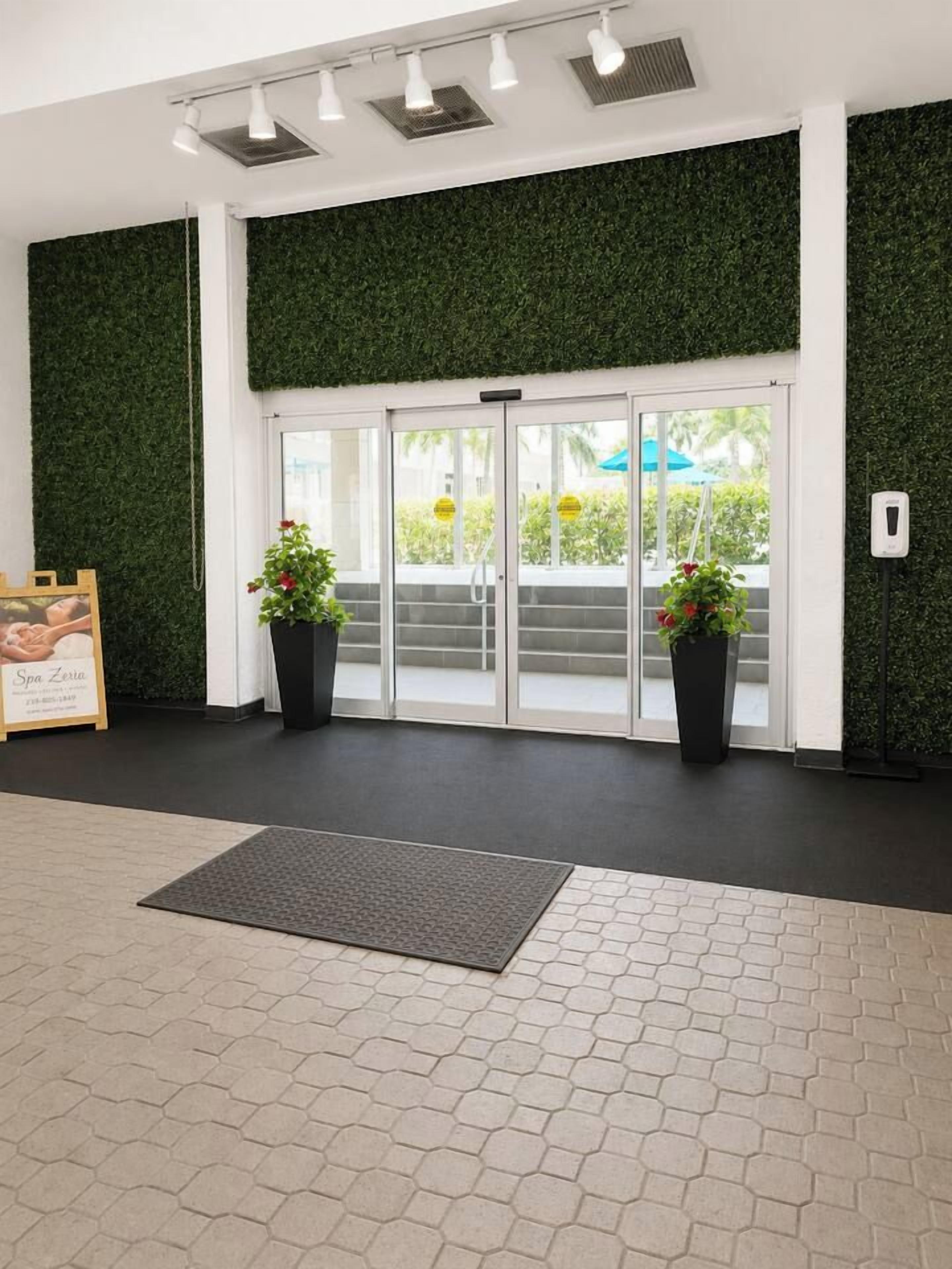 Ein Hotel mit Eingangsbereich, einer grünen Wand, einer Glastür und Topfpflanzen.