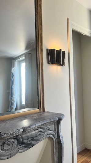 Una habitación con un espejo grande, una lámpara de pared y una chimenea de mármol.