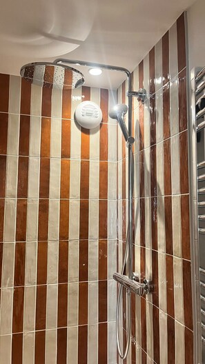 A shower with chrome fixtures and a wall with vertical brown and white tiles. - Faubourg (Paris)
