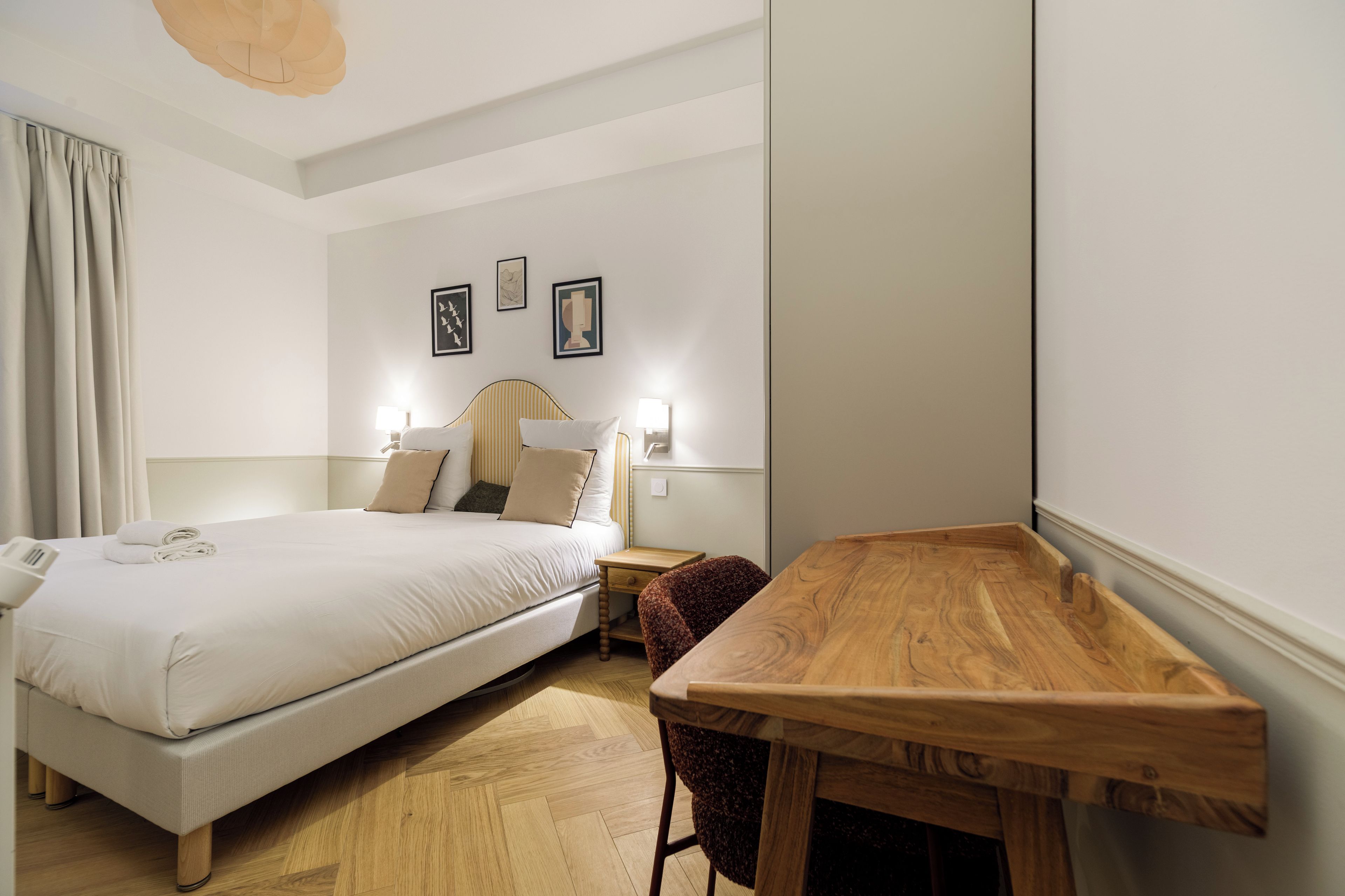 Una habitación de hotel con cama, mesitas de noche, un escritorio de madera y una silla.