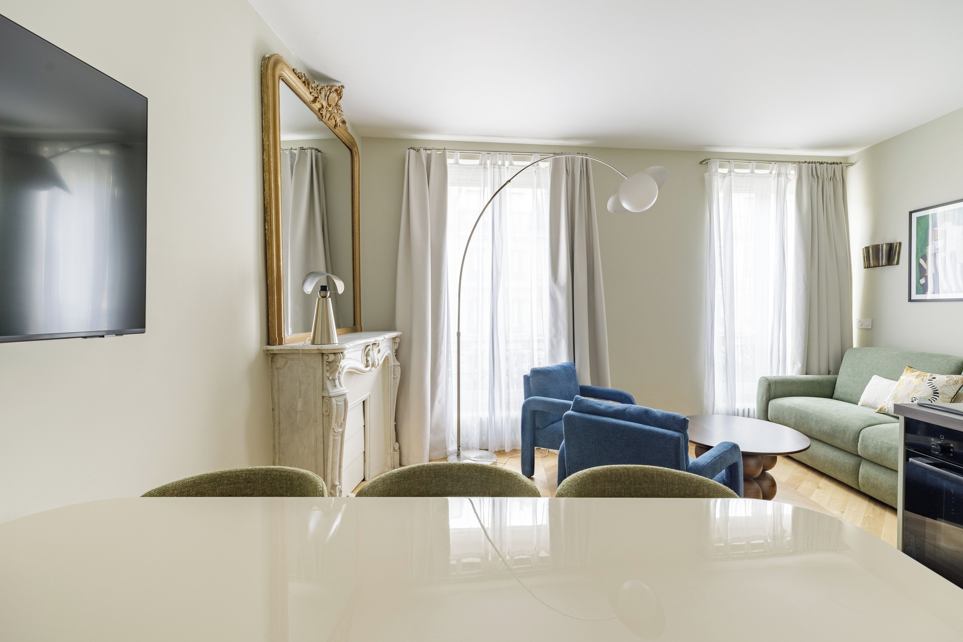 Una sala moderna con una mesa de comedor blanca, sillones azules, un sofá verde y un espejo grande.