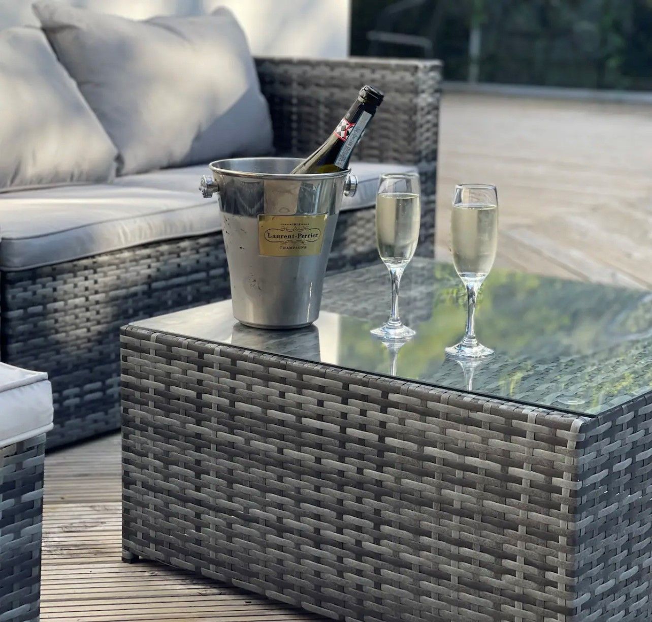Un coin salon extérieur en osier, avec une table en verre, un seau à champagne et deux verres.