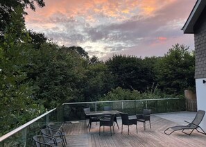 An outdoor deck with a table and chairs, surrounded by greenery and a railing. - Cornwall Holiday Home with hot tub and acre of garden (Saltash)