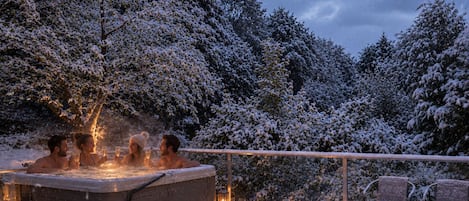 Ein Whirlpool mit Stufen und Laternen, umgeben von schneebedeckten Bäumen.