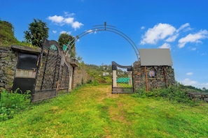 A stone gate with a metal archway leading to a grassy path. - Hotel O Kodaikanal Vilpatti (Kodaikanal)