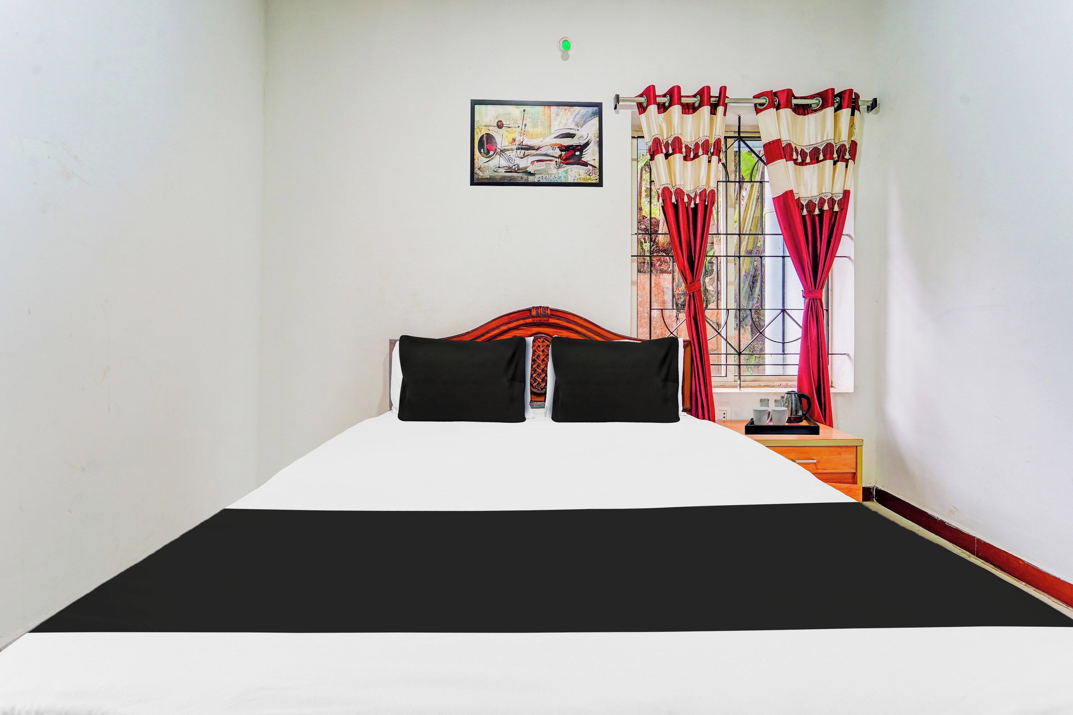 A bed with a black and white bedspread, two black pillows, a wooden headboard, a nightstand with a kettle, cups, and a tray.