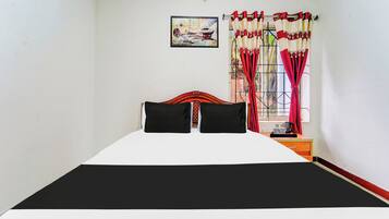 A bed with a black and white bedspread, two black pillows, a wooden headboard, a nightstand with a kettle, cups, and a tray.