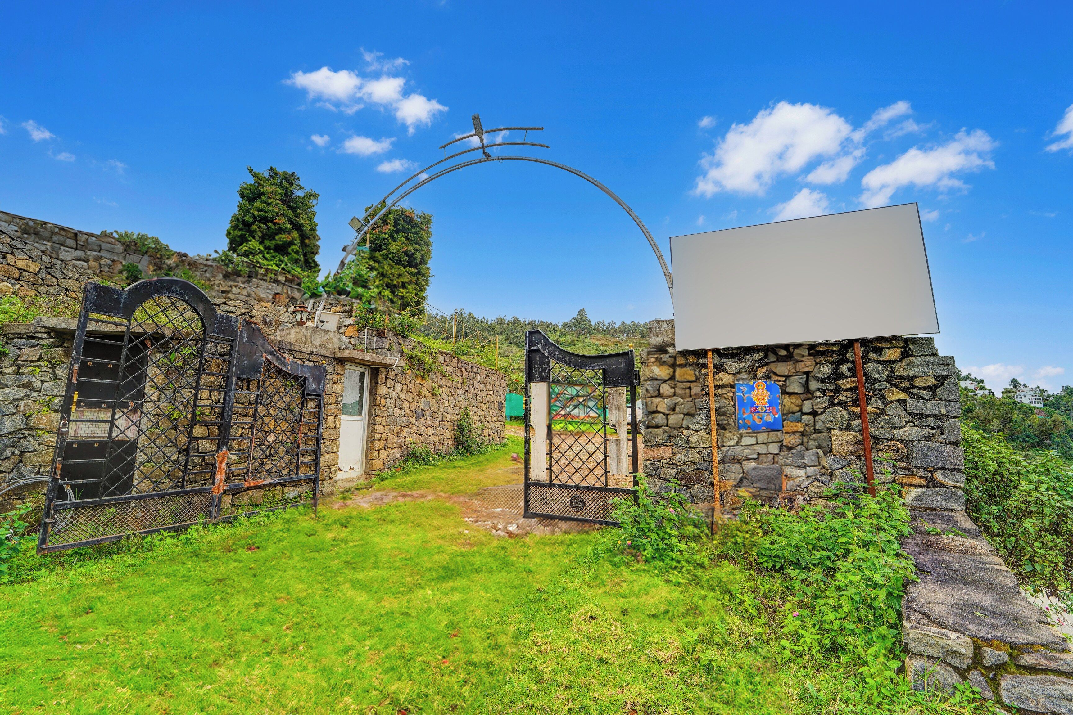 A stone gate with a metal archway leading to a grassy area.