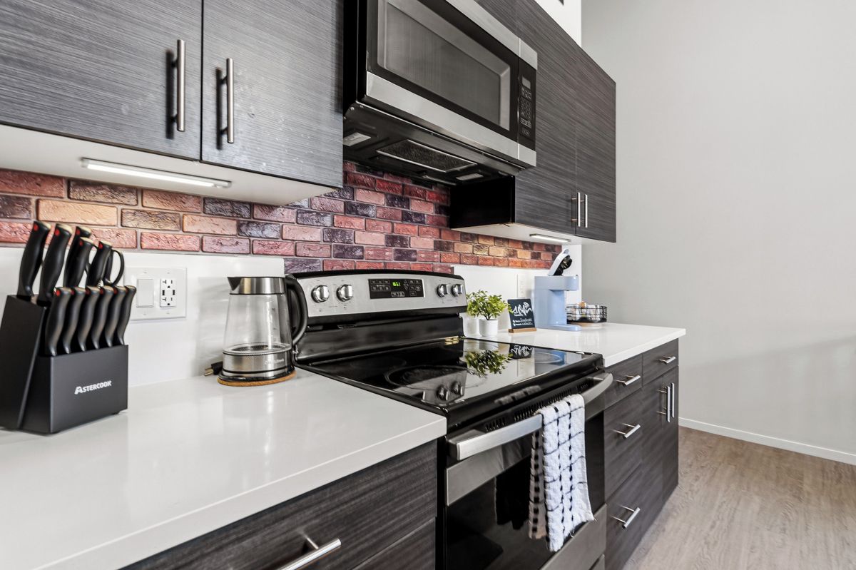 A modern kitchen with a black stove, stainless steel appliances, and a brick backsplash.