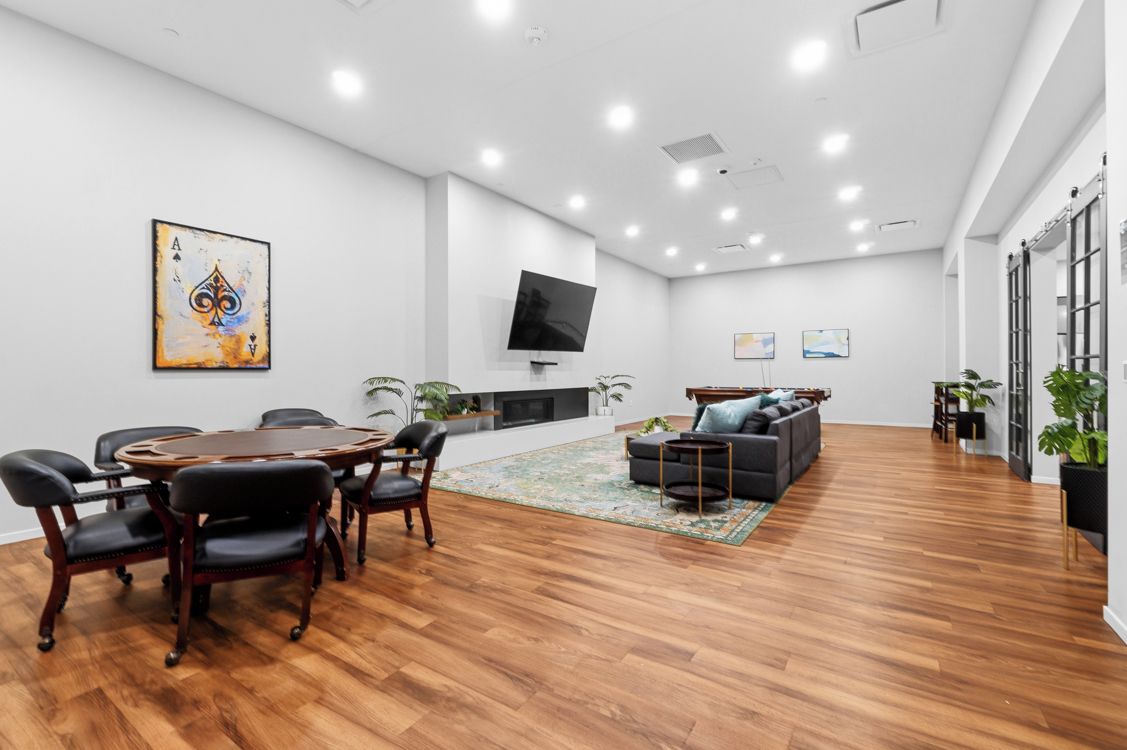 A modern interior with a wooden conference table, black leather chairs, a sofa, and a flat-screen TV mounted on the wall.