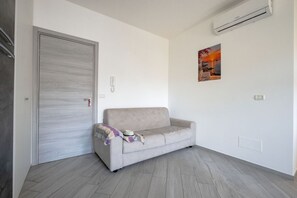 A minimalist living room with a grey sofa, a door, and a wall-mounted air conditioner. - GuestHost - Seaside Bright Apartment with balcony (Bari)
