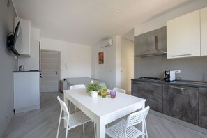 A modern kitchen with white cabinetry, a dining table with chairs, and a small island with a plant. - GuestHost - Seaside Bright Apartment with balcony (Bari)