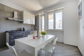 Une cuisine moderne avec une table et des chaises blanches, une cuisinière encastrée et une fenêtre donnant sur la rue.