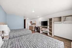 A hotel room with two beds, a desk, a television, and built-in shelving.