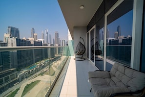 A balcony with a city view, a sofa, and two hanging chairs. - 1 BR Burj Khalifa View at Vera (Dubai)