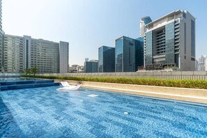 A rooftop swimming pool with a lounge chair, surrounded by high-rise buildings. - 1 BR Burj Khalifa View at Vera (Dubai)