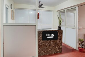 Taulell de recepció d'hotel amb superfície de marbre, un senyal que indica servei de l'empresa i una planta en maceta a la dreta.