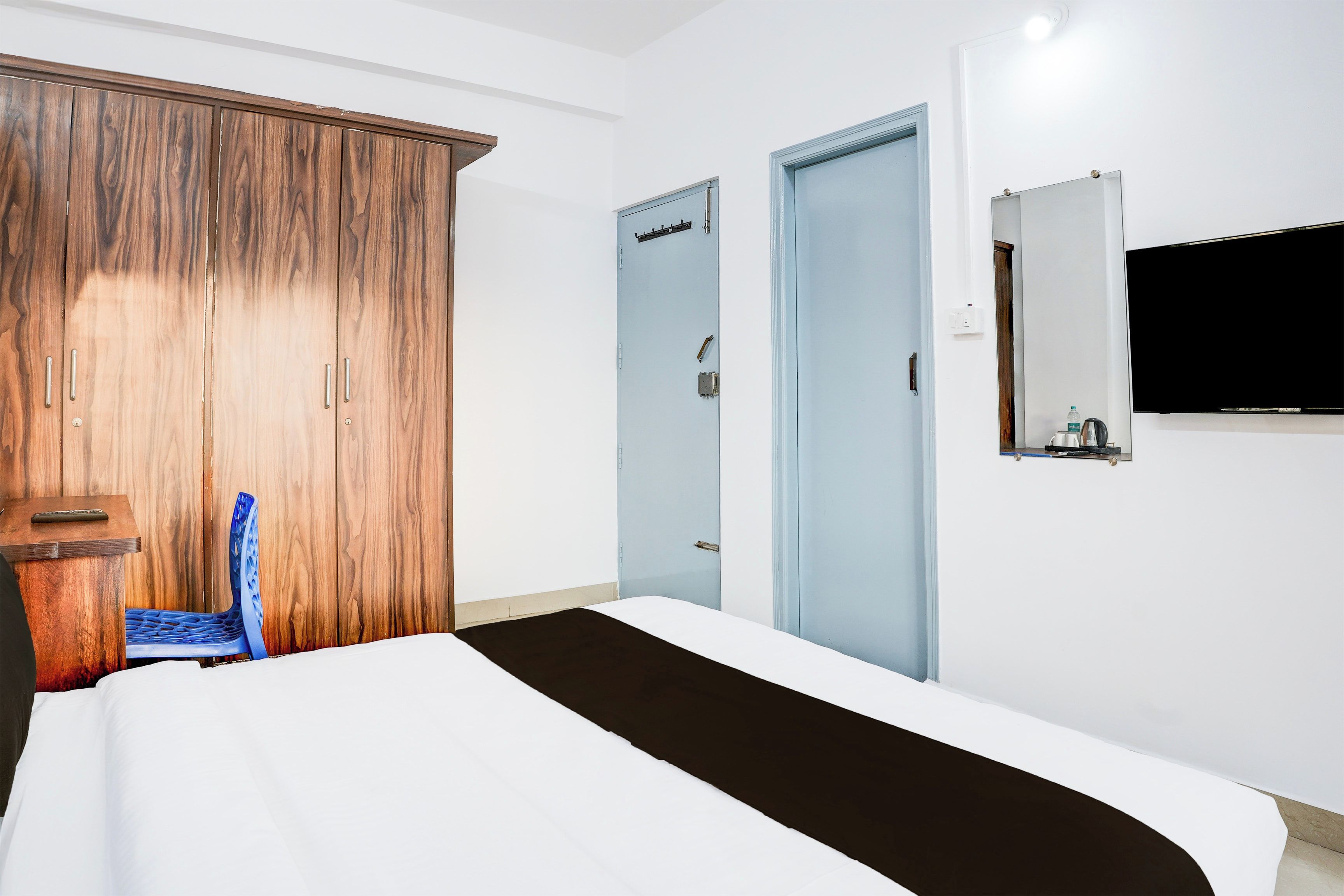 Habitación de hotel con cama, armario de madera, silla azul, escritorio con teclado, televisor de pantalla plana y una puerta.