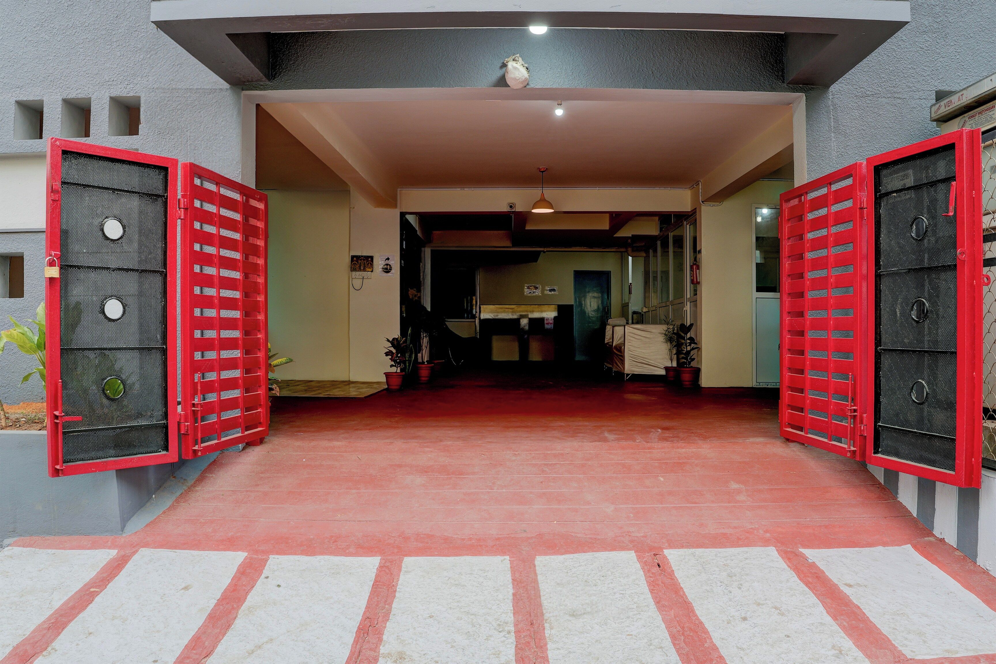 Entrada de un edificio con puertas rojas, suelo de baldosas y una lámpara en el techo.