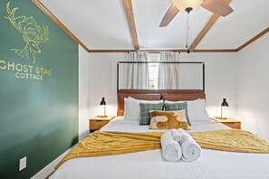 Une chambre d’hôtel avec un lit, des lampes de chevet, un ventilateur de plafond et un mur vert orné d’un logo.