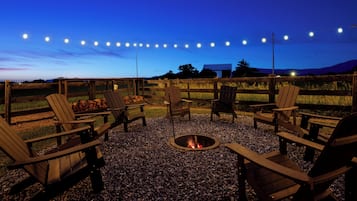 An outdoor seating area with Adirondack chairs and a fire pit, surrounded by a wooden fence and gravel.