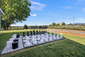 Un jeu d’échecs installé à l’extérieur, sur une pelouse, avec des arbres et une clôture en arrière-plan.
