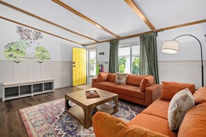 Un salon moderne avec un canapé, une table basse et un banc. On peut voir une porte jaune et une peinture murale.