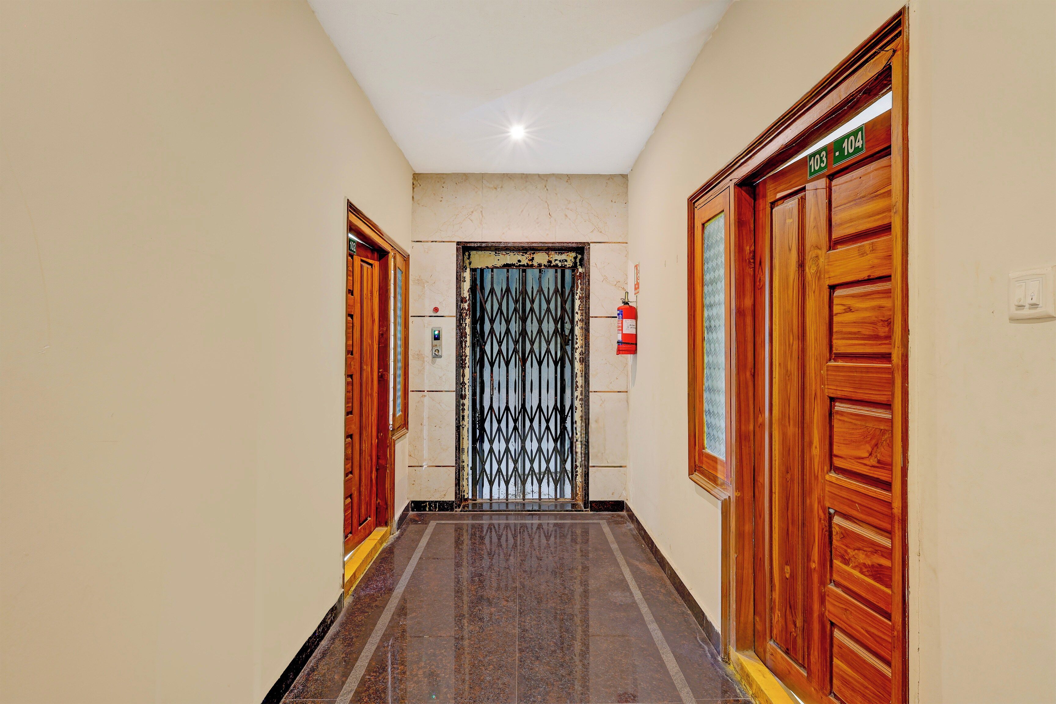 Un pasillo con puertas de madera, un extintor y un cartel con la indicación de las habitaciones 103-104.
