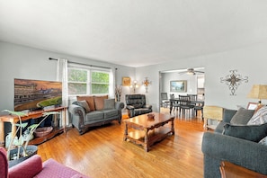A spacious living room with a large flat-screen TV, a fireplace, and a dining area with a chandelier. - Spacious home near Bourbon Trail & Churchill Downs (Louisville)