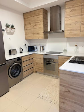 Eine moderne Küche mit Holzschränken, Edelstahlgeräten, einer integrierten Waschmaschine und einer Mikrowelle.
