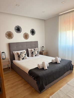 Ein modernes Schlafzimmer mit einem großen Bett, einem grauen Kopfteil und dekorativen Wandbildern.