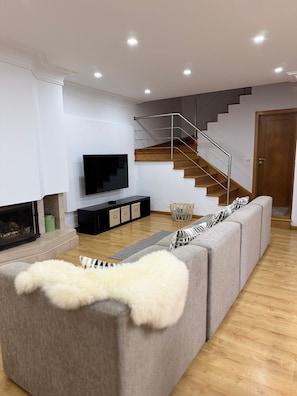 Ein modernes Wohnzimmer mit grauem Sofa, Flachbildfernseher, Kamin und einer Holztreppe.