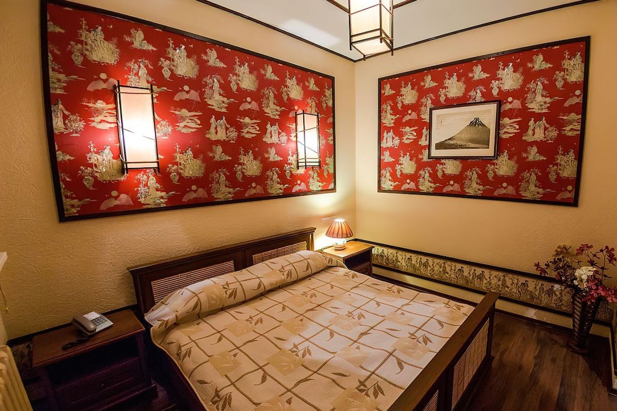 Een hotelkamer met een bed, nachtkastjes, een lamp en een muur met traditionele kunst.